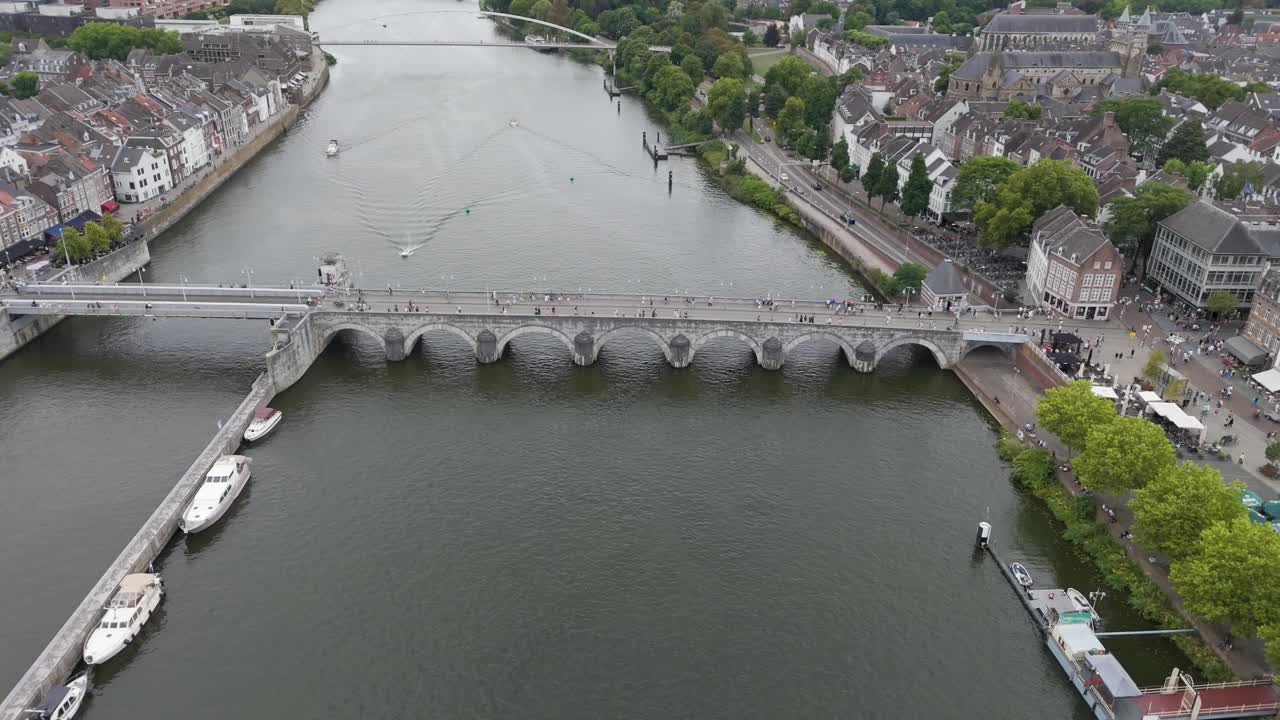 Filmato di un drone dello storico Sint Servaasbrug, un ponte medievale in pietra ad arco che attraversa il fiume Maas a Maastricht. Le viste circostanti includono il centro storico, il lungomare, le barche e il classico arco europeo.