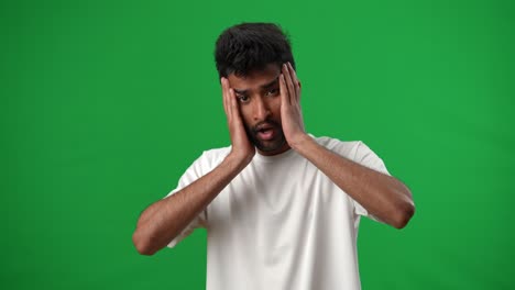 portrait of stressed desperate middle eastern sportsman looking at camera holding head in hands sighing. sad young frustrated footballer posing at chromakey green screen background.