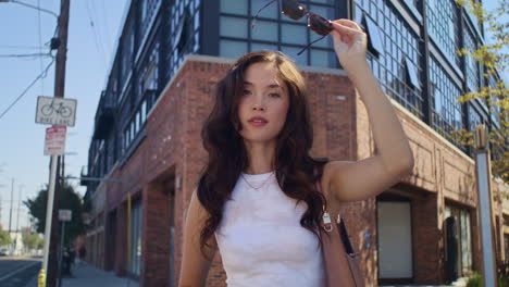 woman take off sunglasses outdoors closeup. asian brunette smiling on camera.