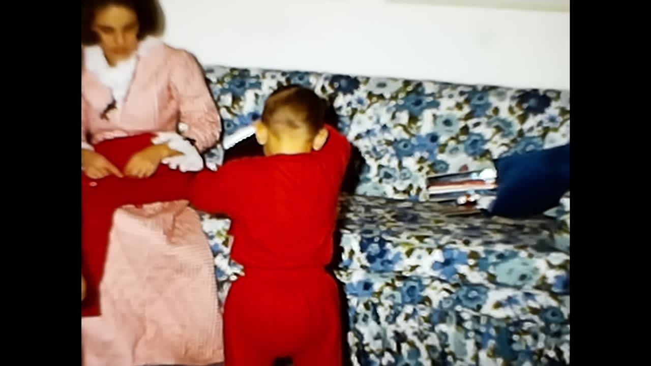 Boy in Red Bathrobe Standing by Christmas Tree. CIRCA USA - 1970s: A boy dressed in a red bathrobe stands next to a festive Christmas tree, creating a nostalgic scene from a 1970s video archive in the USA.