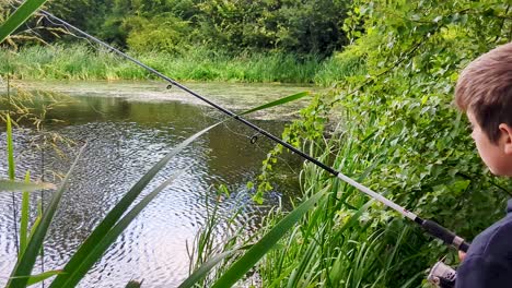 4K-60FPS-Boy-is-Fishing-in-a-Beautiful-Pond-Looking-Through-Cattails---Panoramic-View