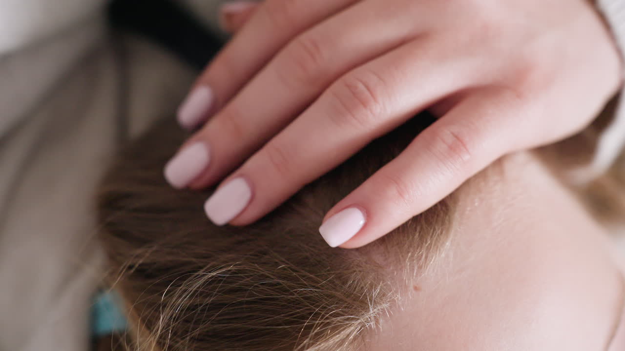 Close up of woman hand gently resting on child head, showing tenderness, comfort, and affection with soft natural light creating intimate family moment expressing bond, care,warmth indoors
