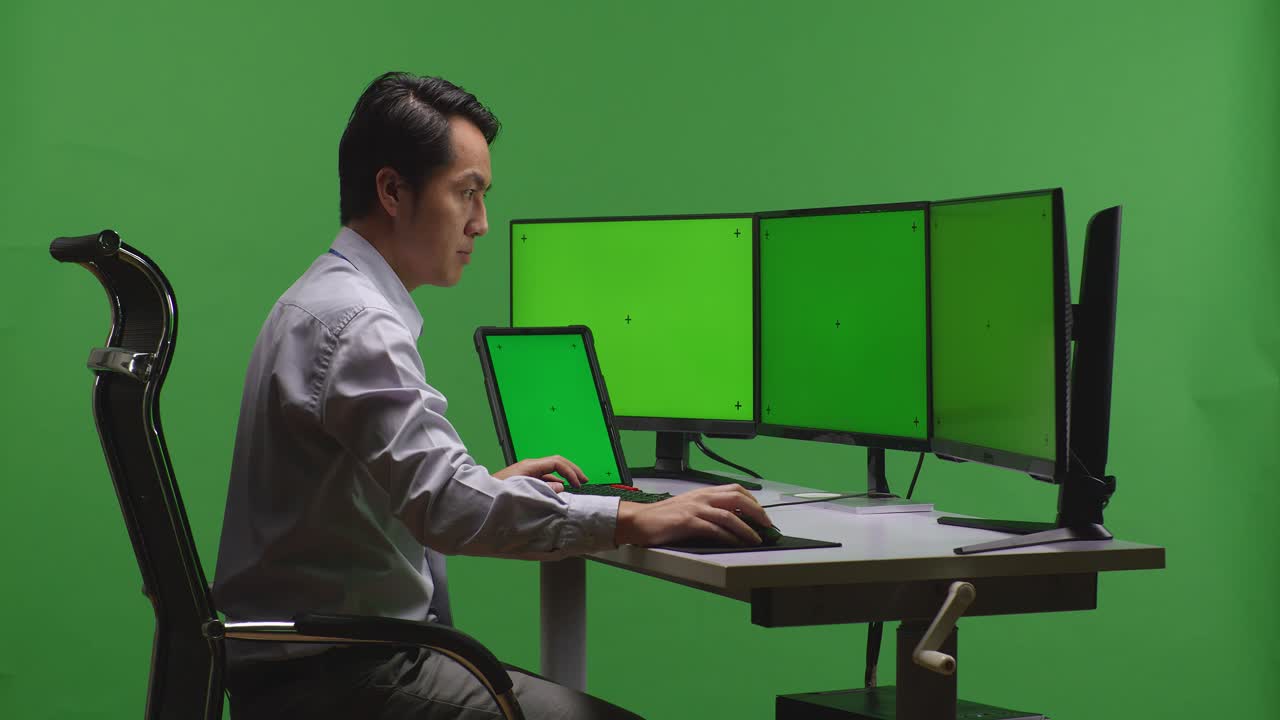 그린 스크린 환경에서 멀티 모니터 책상에서 일하는 사람