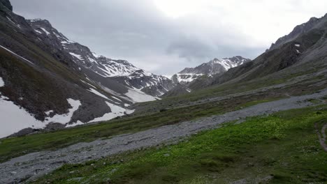 Aerial-drone-footage-flying-through-a-glacial-mountain-landscape-with-patches-of-snow,-isolated-trees-a-remote-alpine-meadows-Switzerland