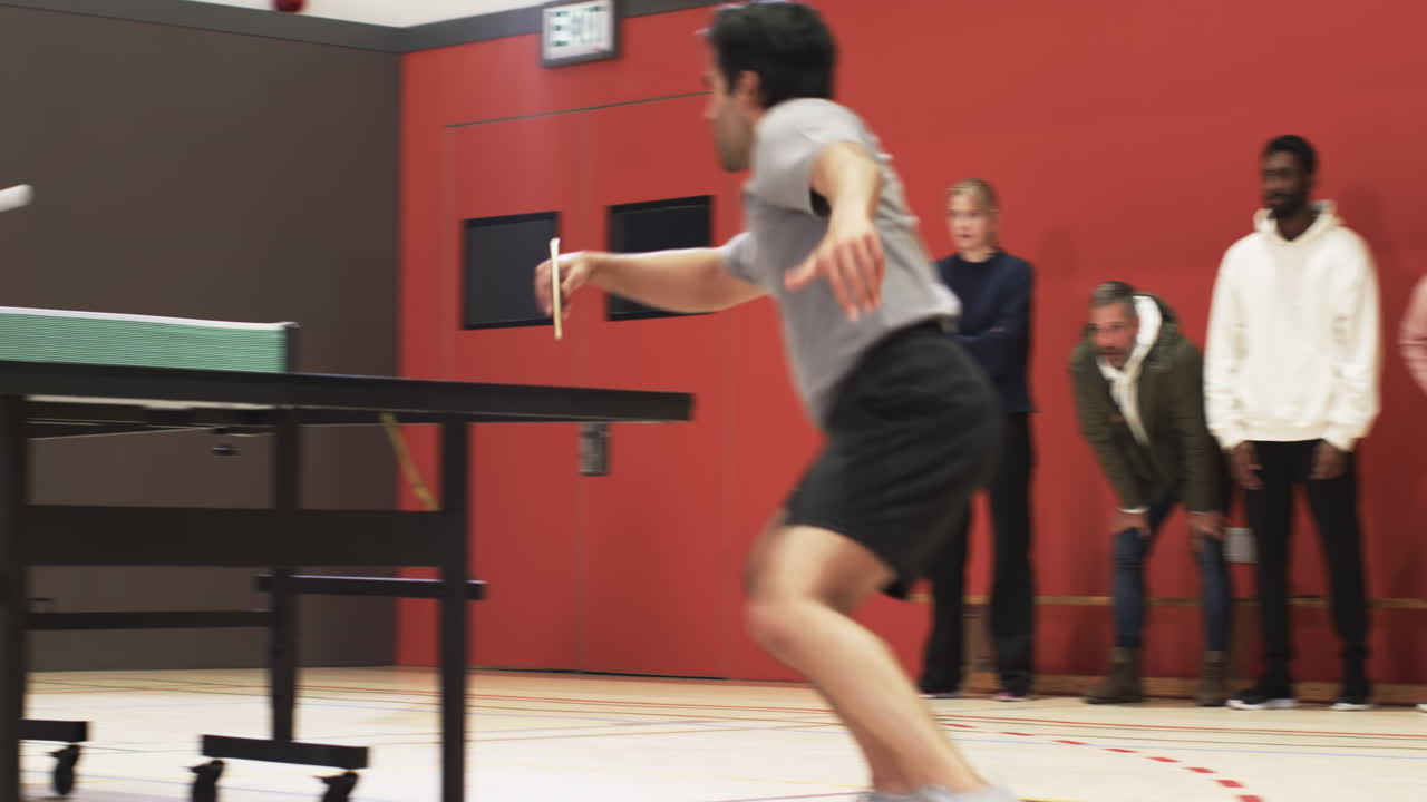 Watching table tennis game, group of people standing and cheering in gym