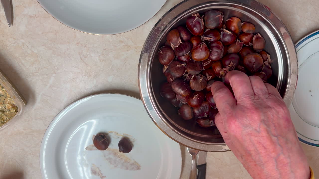 Roasted chestnuts are taken from the bowl by a female hand, she picks some out, tilt down shot