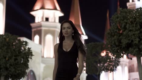 mujer con vestido negro caminando por la noche frente a un castillo