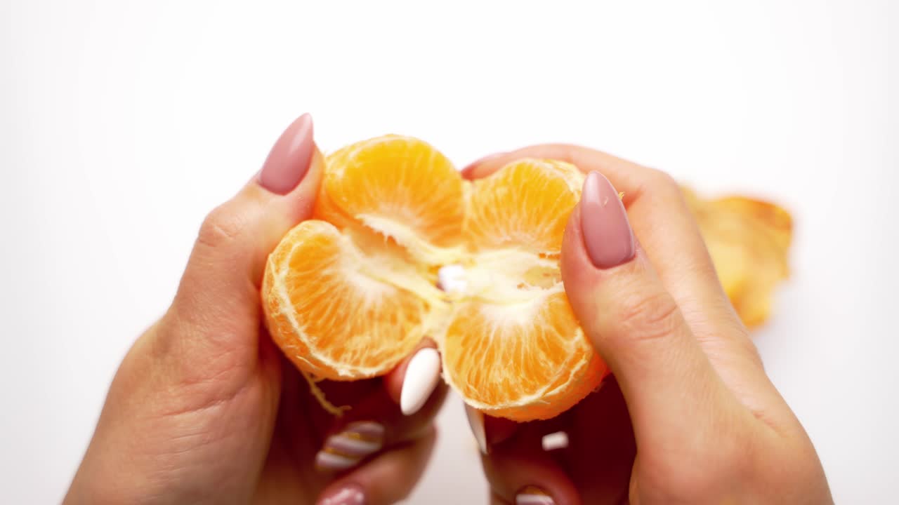 Orange mandarin in woman's hands. Hands are peeling a juicy fruit on white background. Close-up.