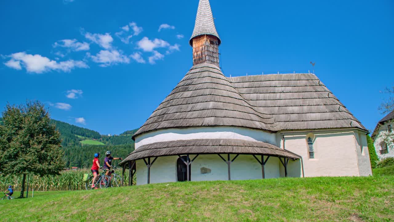 Reveal of church Saint John the Baptist at Muta. Happy couple bikers pass by