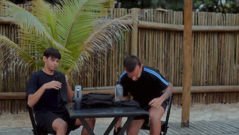 two men packing or organizing items at an outdoor table in a tropical setting