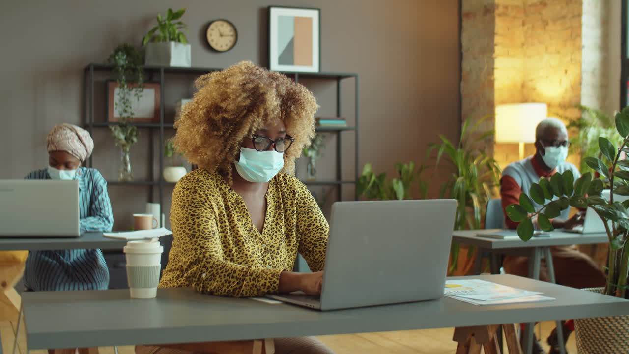 mujer de negocios afroamericana con máscara trabajando en la oficina