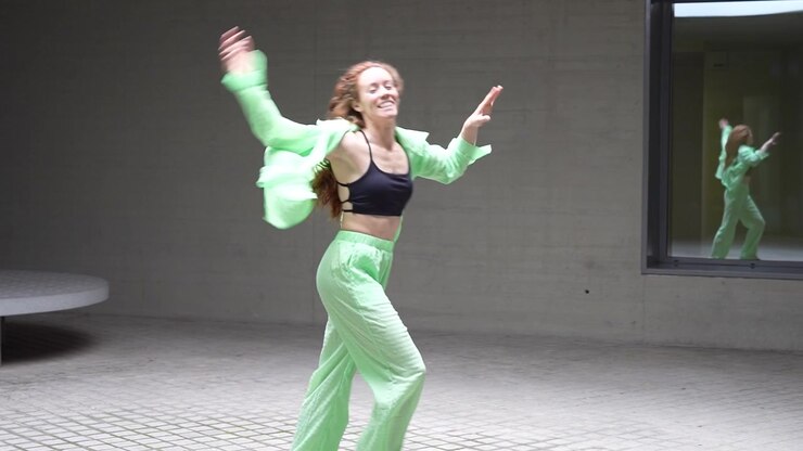 A young woman wearing a green outfit is dancing energetically in an urban environment