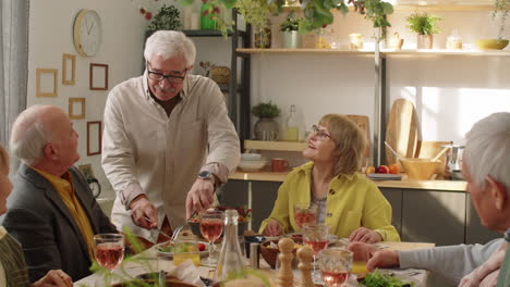 senior man serving meat on plates for friends at home dinner