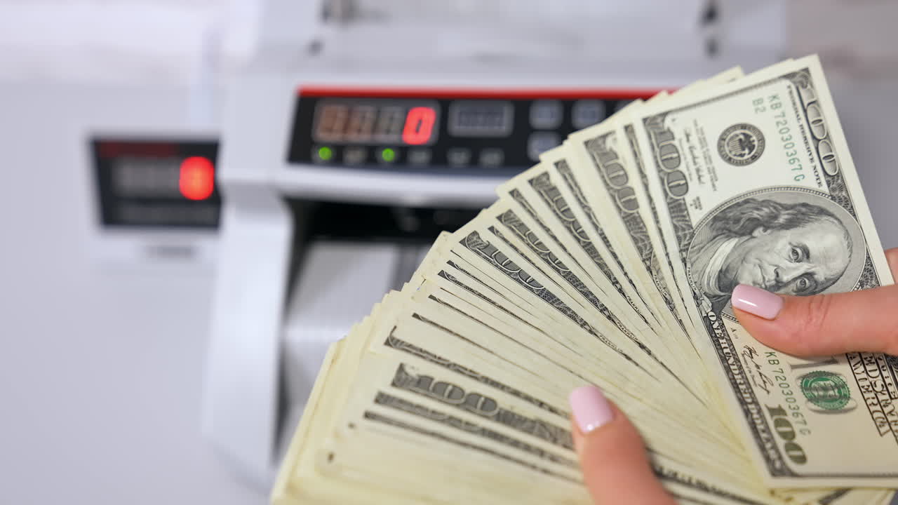 Woman holding money near counting machine at table indoors, closeup