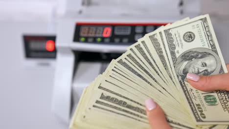 woman holding money near counting machine at table indoors, closeup