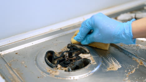 cleaning a stove with care and precision. a person wearing a glove scrubs a dirty stove top, effectively removing grease and grime