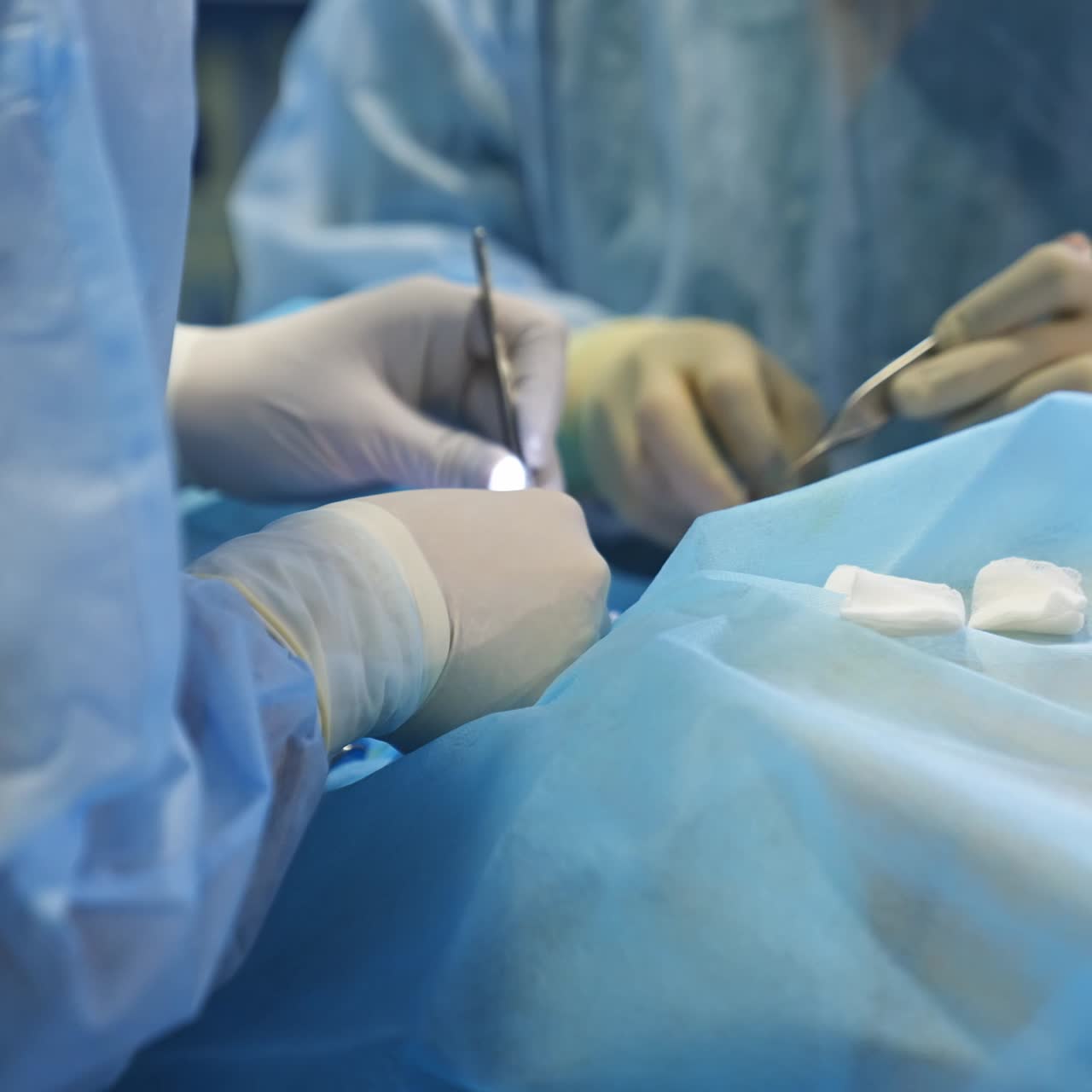 Hands in latex gloves of surgeons operate the patient with metal tools. Doctors stack the used instruments on the table nearby. Close up