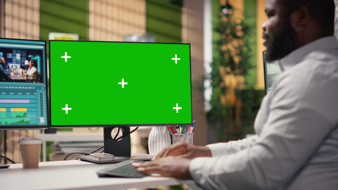 Afroamerikansk mand arbejder ved computer med green screen-skærm