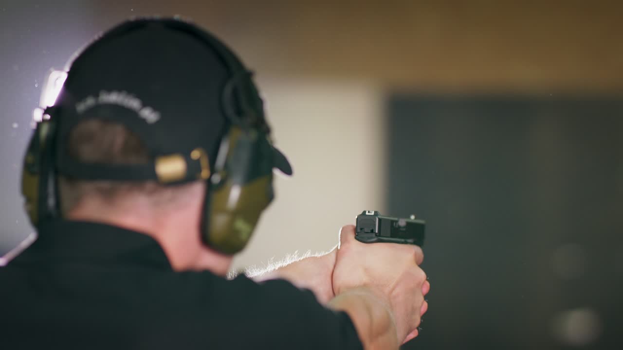 vista de atrás de un hombre que devuelve una pistola a su funda después de disparar un disparo en un campo de tiro interior