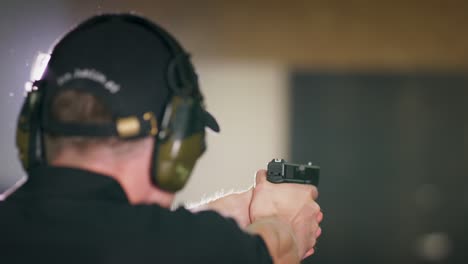 back view close-up of a man returning a pistol to its holster after firing a shot at an indoor target range