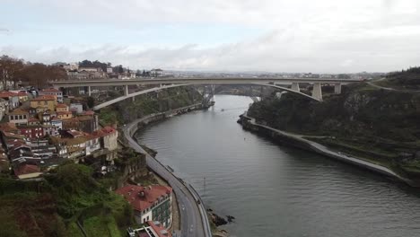 drone footage of multiple bridges over douro river in porto, portugal with riverside roads, hillside houses, and overcast sky creating a calm scenic view of this urban landscape