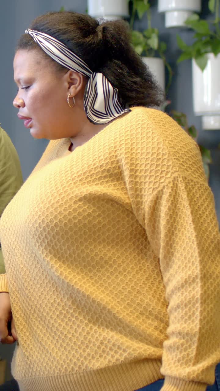 Vertikal video: Ved mødestart taler kvinde i sennepsgul sweater i et hjørne, med plads til tekst.