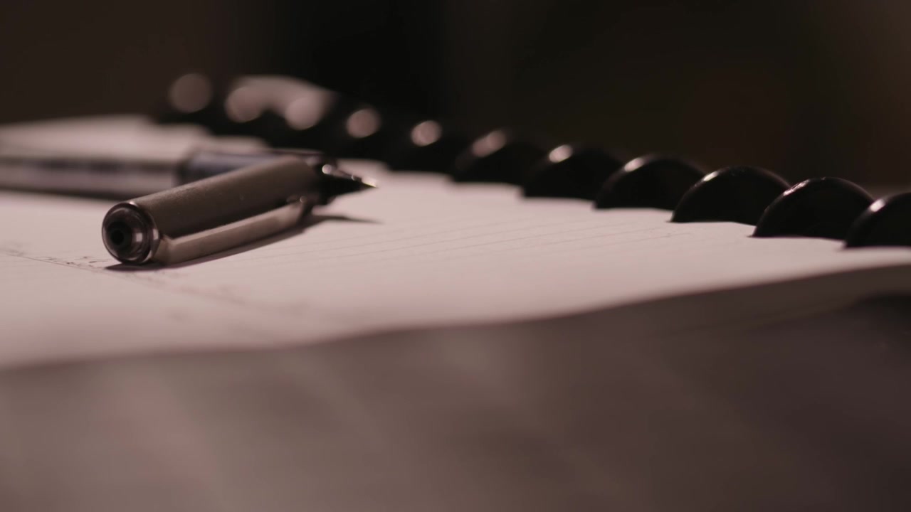 Fingre, der skriver på et tastatur i den slørede forgrund, med en kuglepen og en notesblok i fokus i baggrunden.