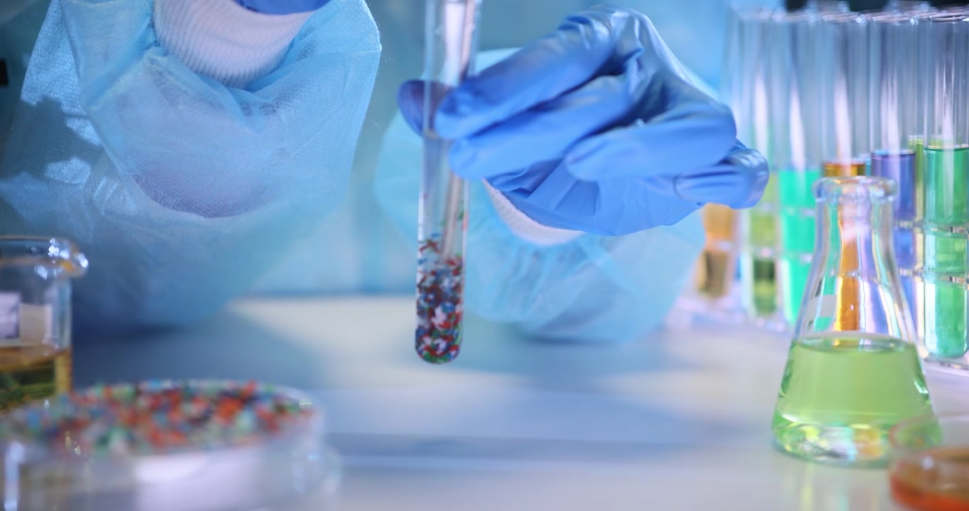 Chemist hands stir particles of microplastic in test tube