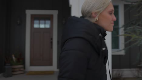 woman walking outside the front door of a house to walk to her car in the driveway and getting in