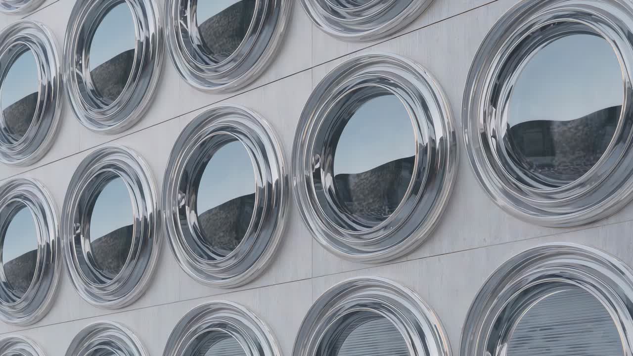 Panning camera moving across chrome porthole window grid on light panels, showing ridge reflections