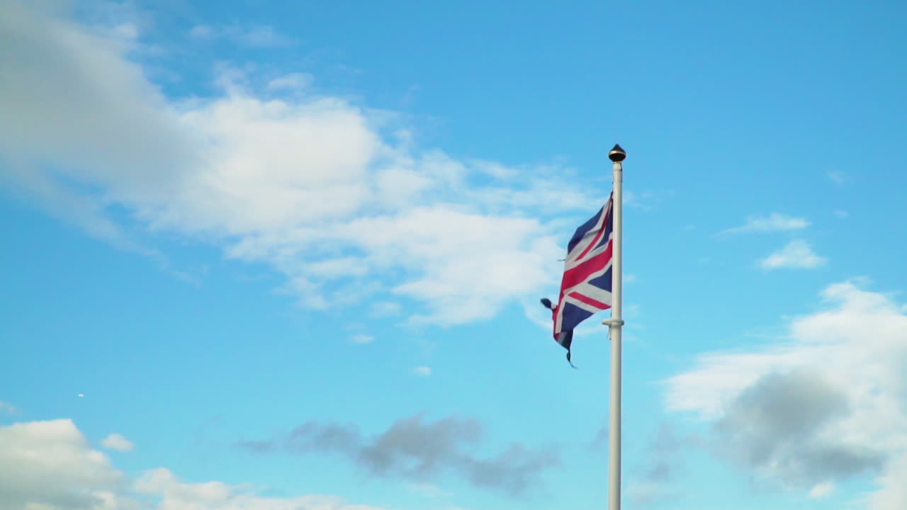 Bandiera Union Jack strappata che sventola al rallentatore contro un cielo blu
