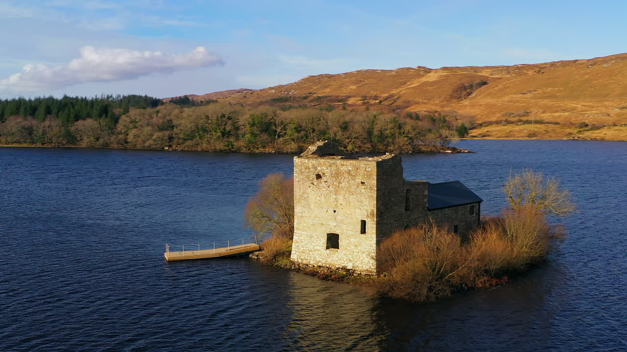 Aerial orbit of O’Flaherty Tower House on Ballynahinch Lake, framed by Connemara’s mountains in soft light