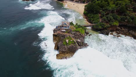 Bird-eye-drone-shot-of-coral-island-on-the-beach-in-big-sea-wave---Kukup-Tropical-Beach,-Yogyakarta,-Indonesia