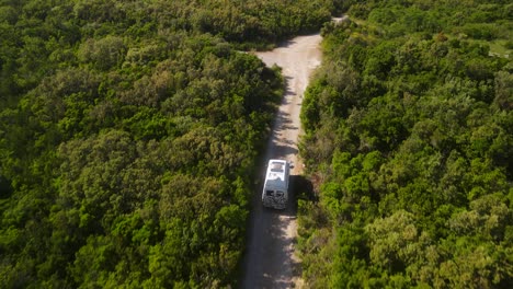 RV-traveling-on-gravel-road-surrounded-by-green-forest