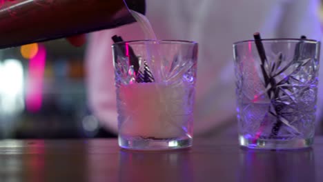 bartender pouring tropical cocktail from steel shaker on bar counter, close up