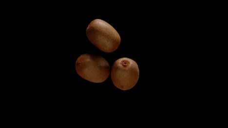 Bunch-of-kiwi-fruit-falling-down-isolated-on-black-background,-super-slow-motion-view