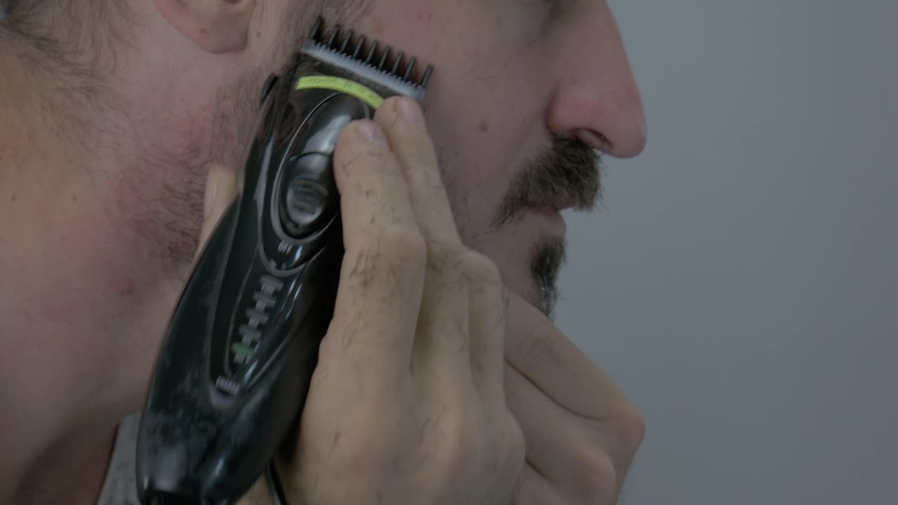 un hombre está recortando su cabello facial con una afeitadora eléctrica para verse bien