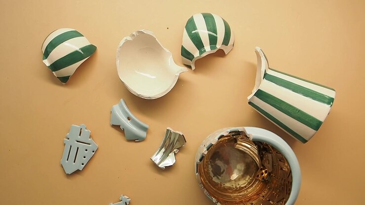 Broken Pieces of a Striped Ceramic Vase on a Beige Surface