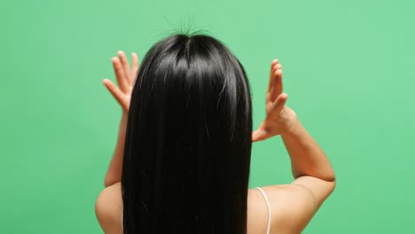 close up back view of a woman putting her long and black straight healthy hair up in ponytail in the green screen background studio