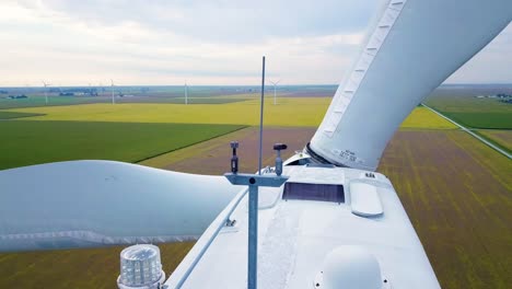 Close-up-aerial-view-behind-rotating-wind-turbine-blades-and-weather-measuring-equipment-on-green-countryside-farmland