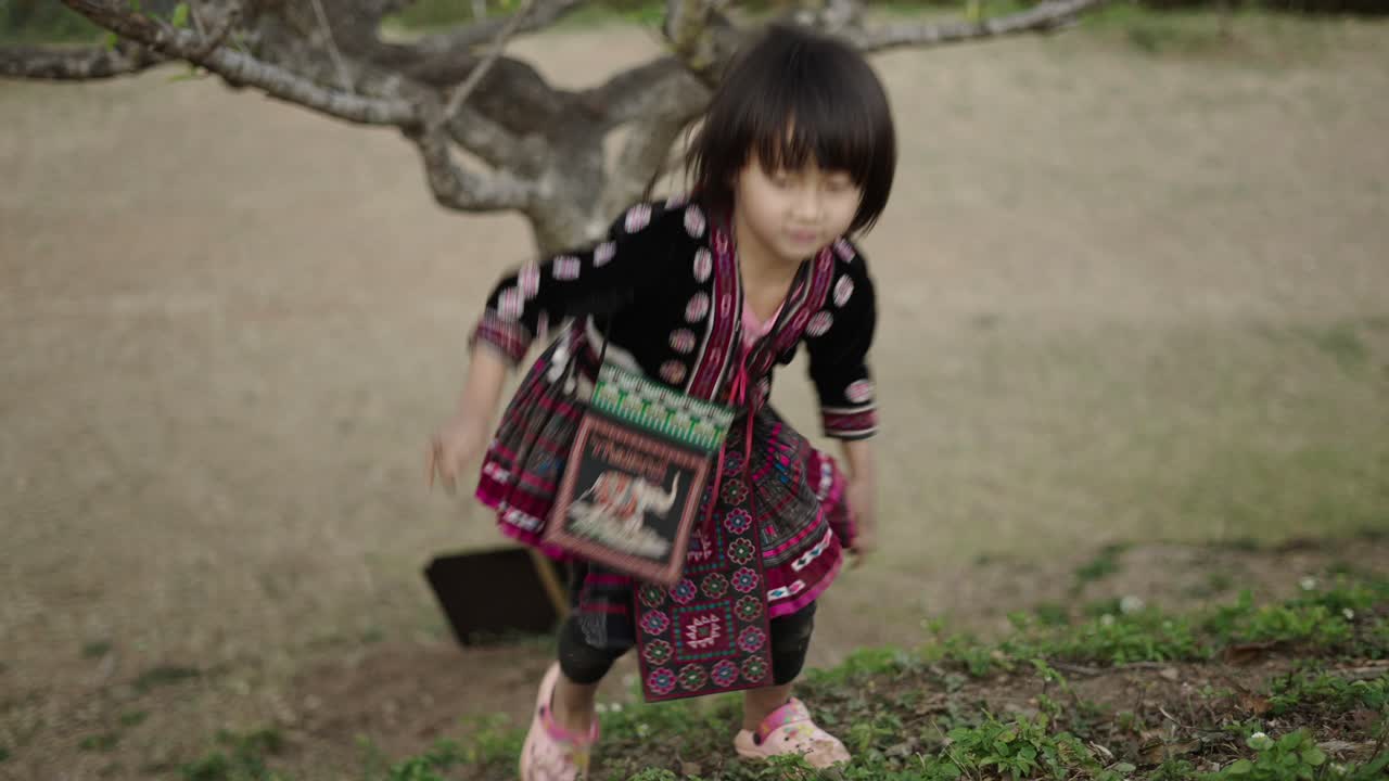 Young Girl in Traditional Attire Climbing a Grassy Hill