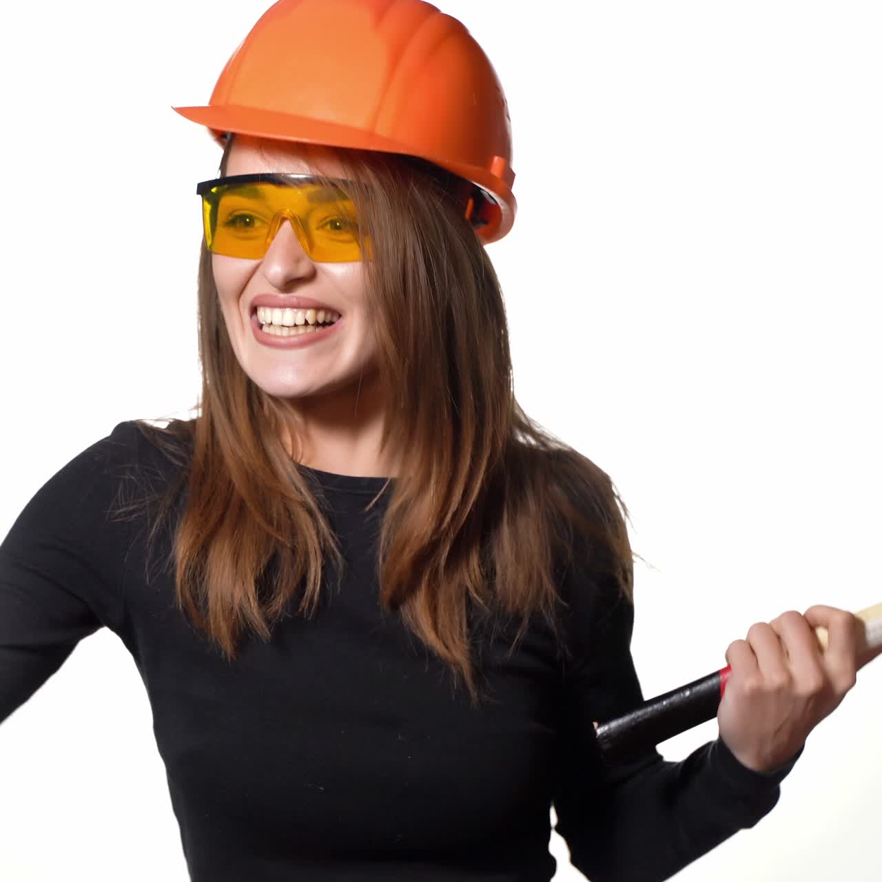 A pretty woman with orange helmet and eyeglasses is posing with a pickaxe in her hands on a white background in the studio. Profession of engineer