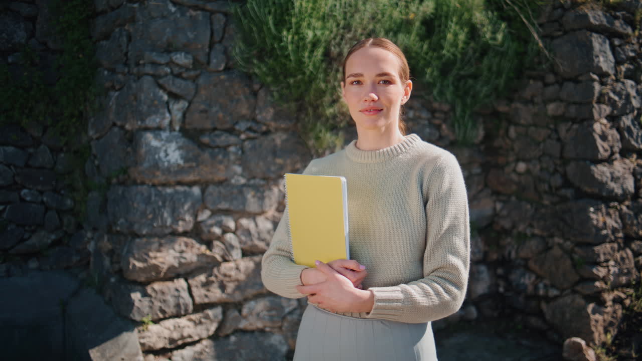 Student girl carrying books waiting at sunny place closeup. Woman looking camera