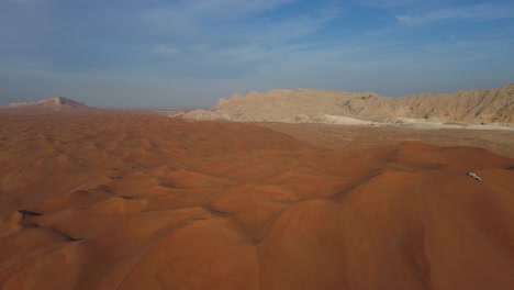 UAE-Desert:-Top-View-of-Sharjah-Desert,-A-group-of-4x4-vehicles,-rides-on-Giant-Sand-Dunes,-Mleiha-Mountains-in-the-Background