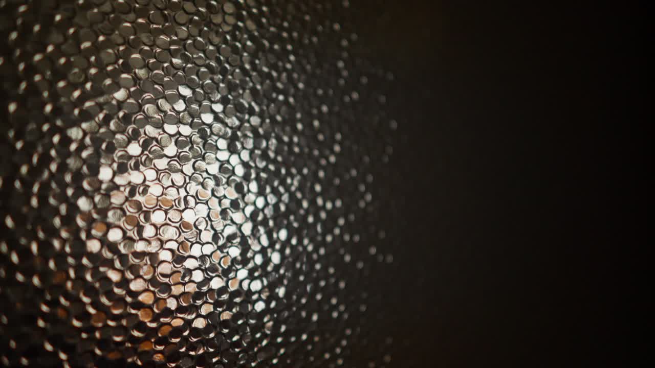 Suspended mosaic glass ball sways under spotlight with dark background