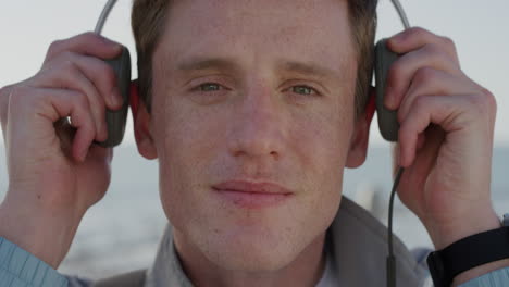 close up portrait young man student puts on headphones enjoying listening to music realxing on seaside red head male teenager freckles slow motion