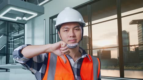 primer plano de un ingeniero masculino asiático con casco de seguridad mostrando el pulgar hacia abajo y sacudiendo la cabeza mientras está de pie con el proyecto de drones