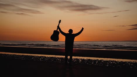 hombre corriendo con guitarra en la playa de arena trasera al atardecer-9