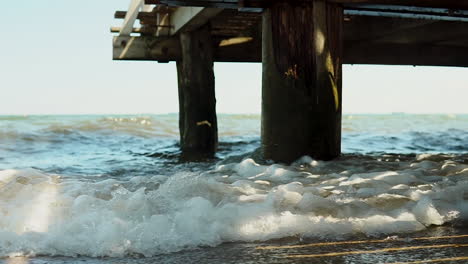 Turbulente-Wellen-Auf-Dem-Meer-Werden-Vom-Pier-Reflektiert,-Wasser-Trifft-Auf-Die-Ins-Meer-Gerammten-Holzpfähle,-Das-Wasser-Bildet-Schaum-Und-Es-Kommt-Zu-Einer-Großen-Wasserbewegung