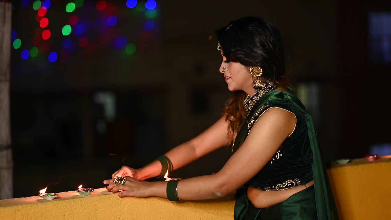 Bella giovane donna che accende una diya (lampada a olio) in abiti tradizionali in occasione del Diwali.